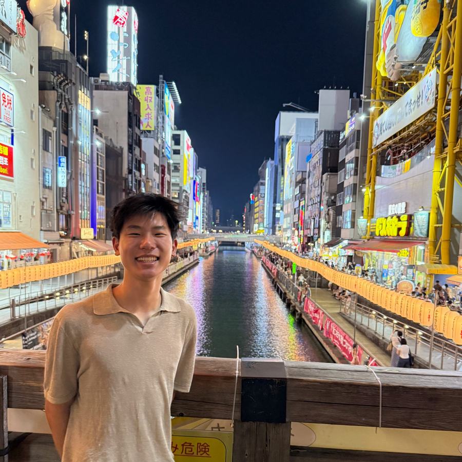 Ethan on a bridge over the Dotonbori canal in Osaka at night, lined with neon signs and lanterns