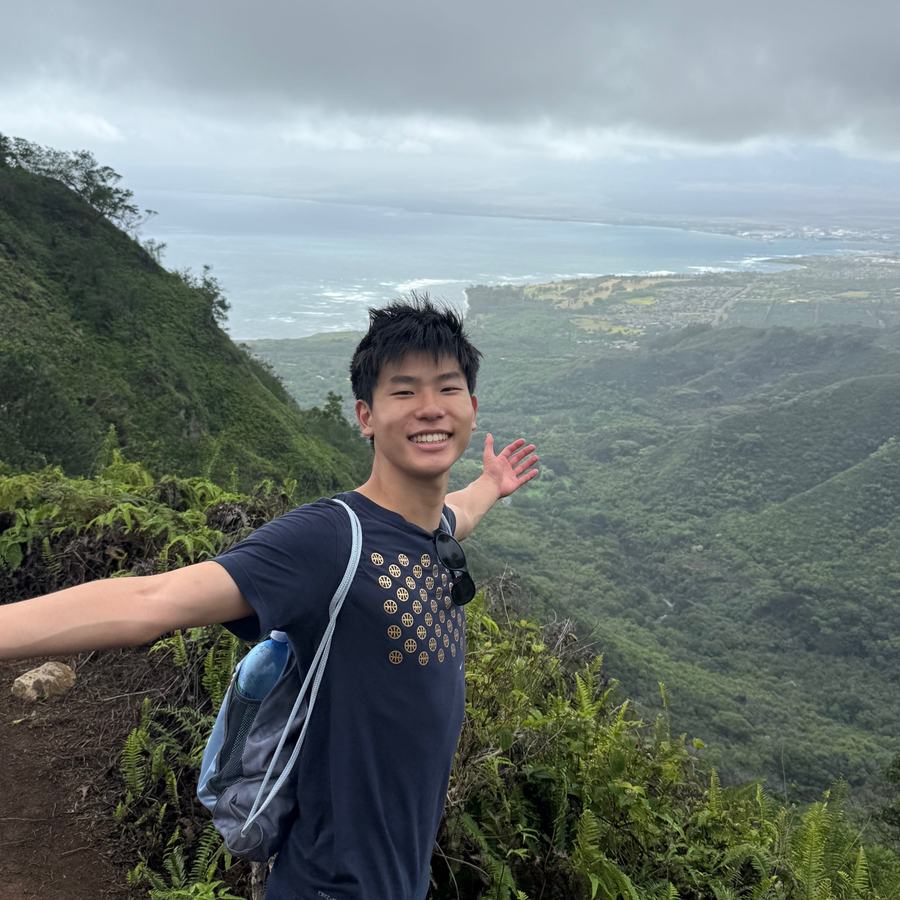 Ethan with his arms spread on a green mountain ridge trail above the coast in Hawaii