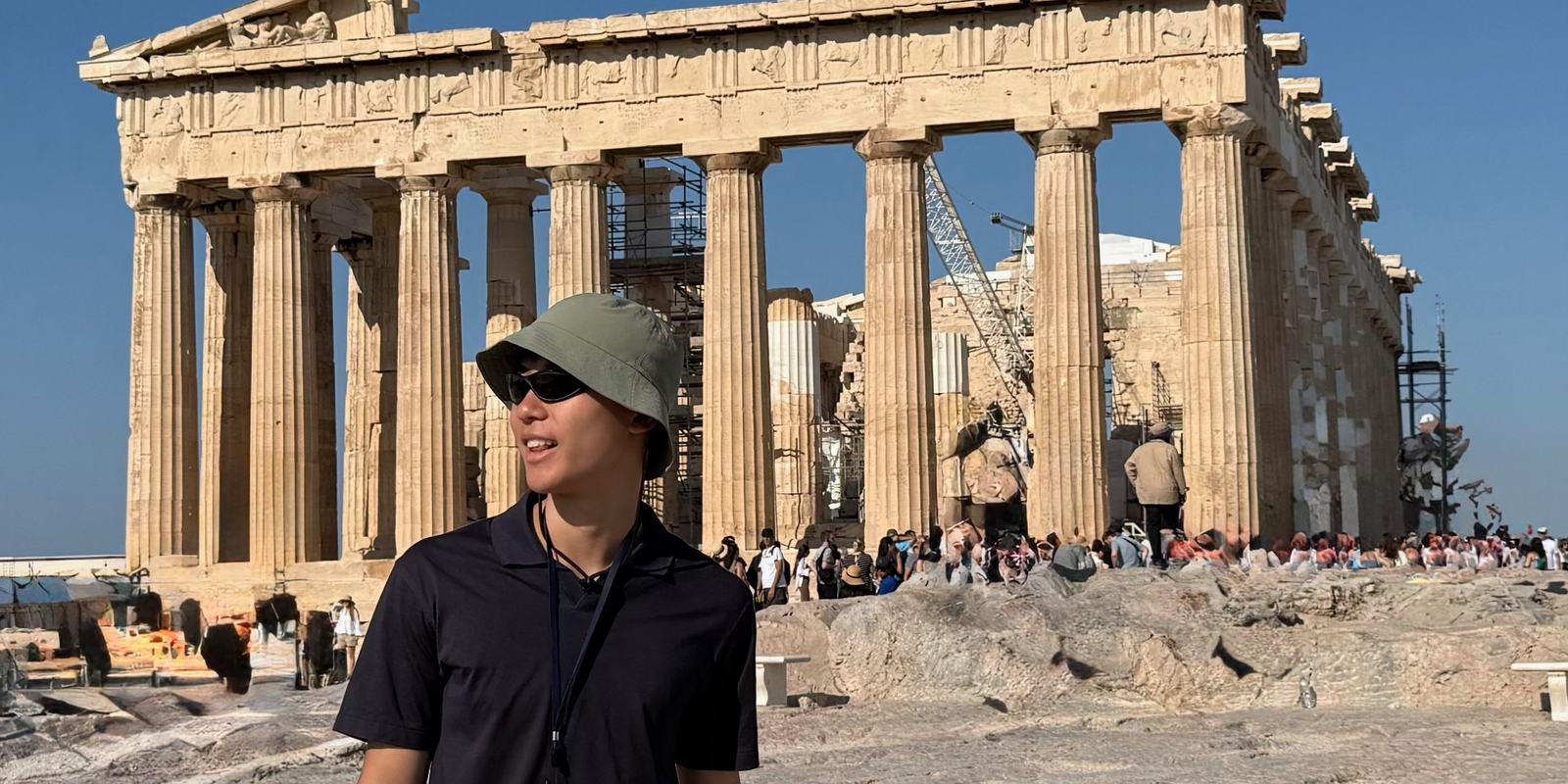 Ethan in a bucket hat and sunglasses walking past the Parthenon in Athens