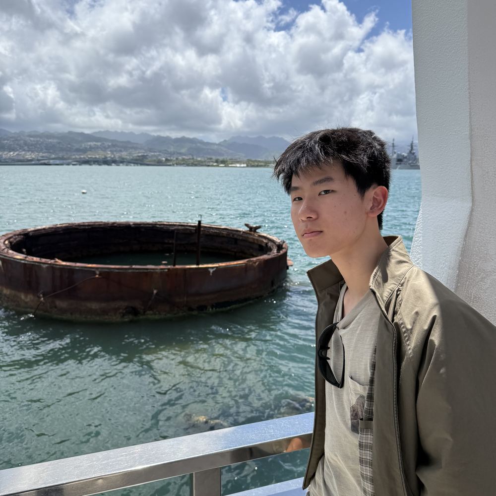 Ethan at the USS Arizona Memorial, with the rusted gun turret base of the sunken battleship visible in the water behind him