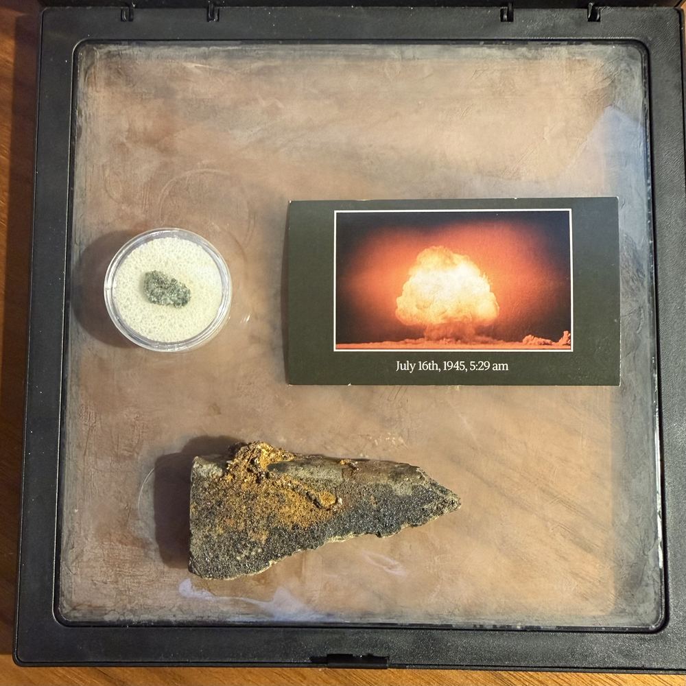 A display case with a roof tile fragment, a small sample of trinitite, and a photo of the first atomic test dated July 16, 1945