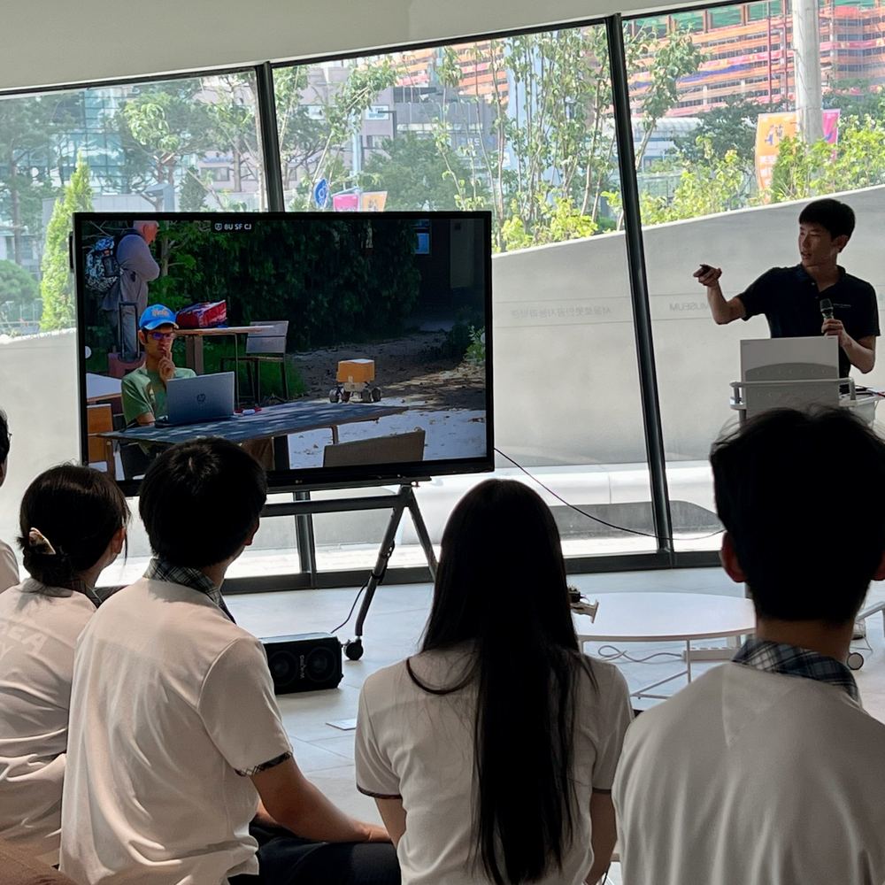 Ethan pointing to a video of Food Angel driving through a park during his talk in Seoul